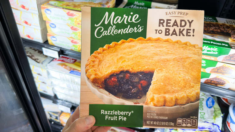 Someone holding a frozen Marie Callender's Razzleberry Fruit Pie in a grocery store freezer aisle