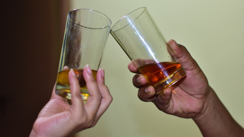 Two hands clinking glasses filled with different whiskies