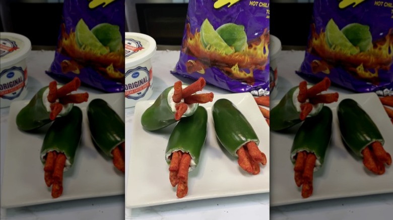 Takis filled jalapeño poppers on white plate with Takis and cream cheese in background