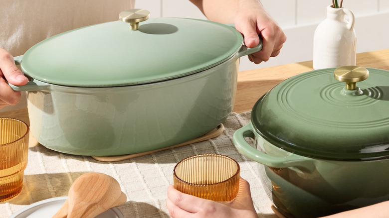 A person placing a sage green Best Choice Products Oval Cast-Iron Dutch Oven on a kitchen counter