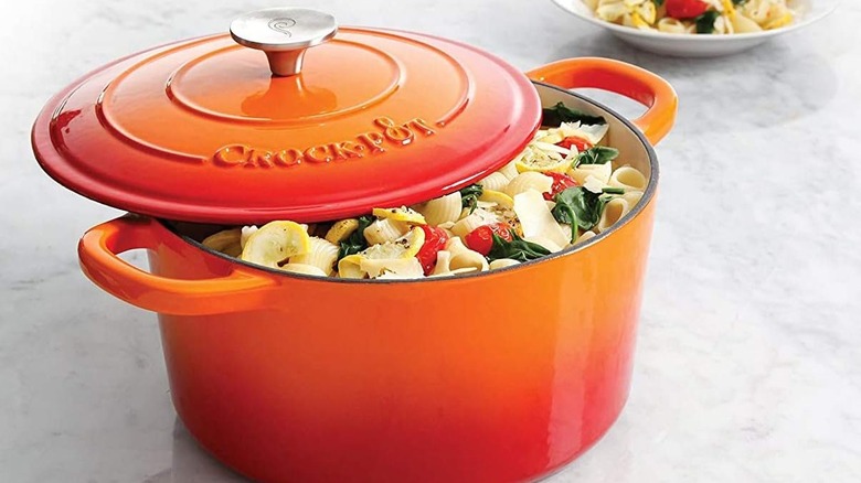 An orange Crock Pot Artisan Round Enameled Cast Iron Dutch Oven on a kitchen counter
