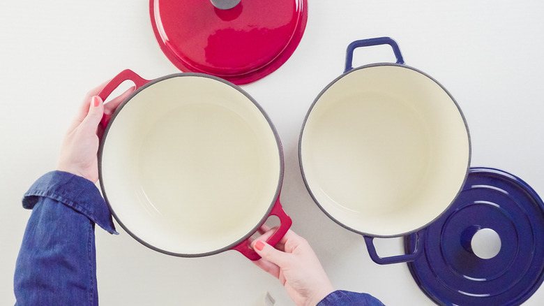 A person placing an enameled cast iron Dutch oven next to two other pieces of cookware