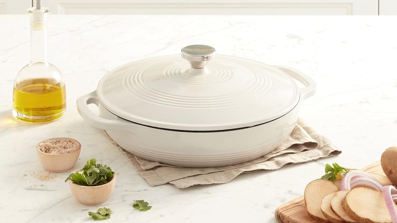 A white Lodge Essential Enamel Braiser on a kitchen counter surrounded by ingredients