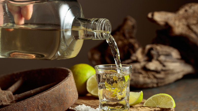 hand pouring tequila shot on wood surface