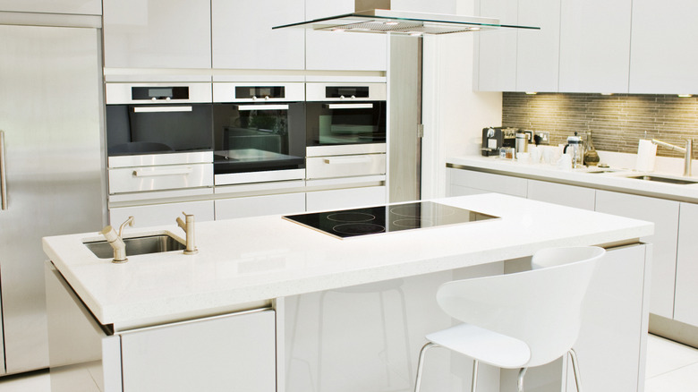 A white countertop in a sleek, modern kitchen with an island, multiple ovens, and two sinks