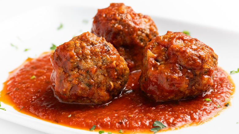 three meatballs sit in a pool of marinara sauce on a white plate scattered with herbs.