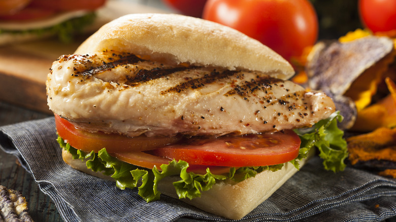 A grilled chicken sandwich on bread with lettuce and tomato sits on a napkin.