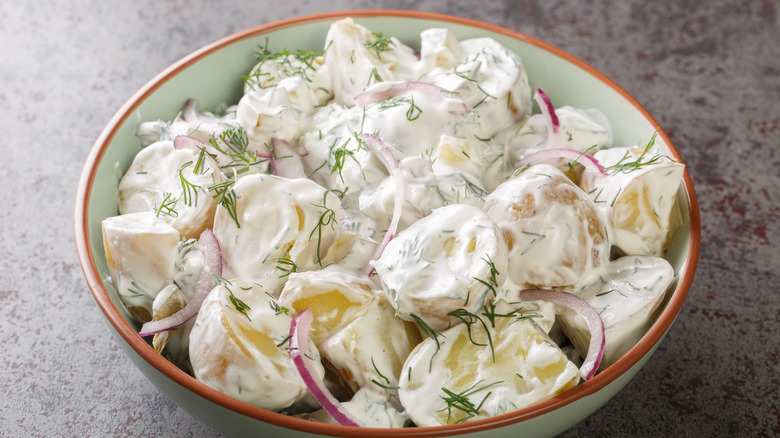 creamy potato salad in a white bowl with red onions and fresh herbs