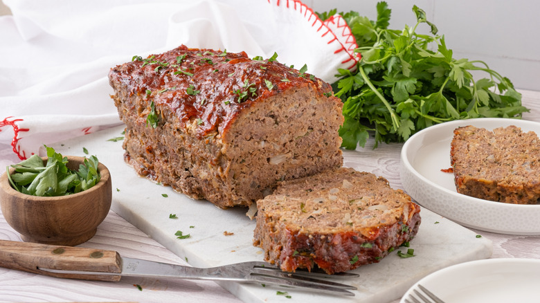 Meatloaf with slice, parsley, fork on cutting board
