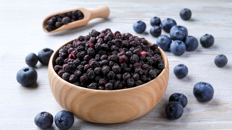 dried and fresh blueberries in a wood bowl and scoop on a white surface