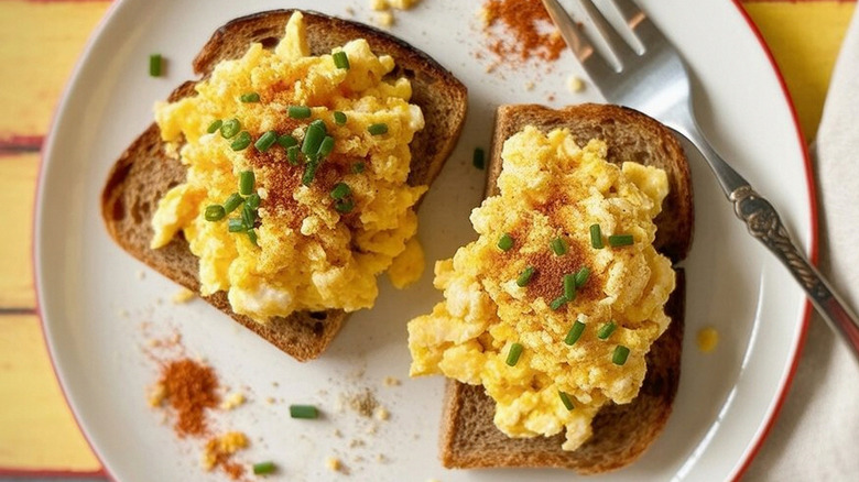 Scrambled eggs over toast with seasoning and chives, on a plate with fork