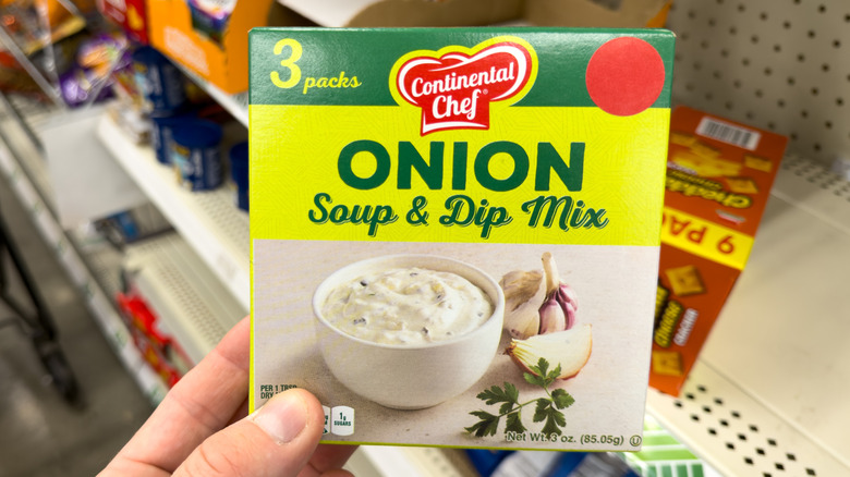Hand holding box of Continental Chef Onion Soup & Dip Mix in front of grocery store shelf