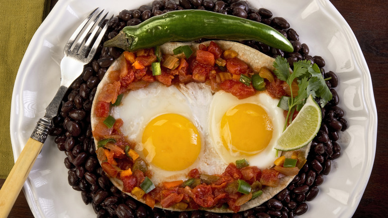 Eggs on a tortilla with salsa, black beans, chilies and lime