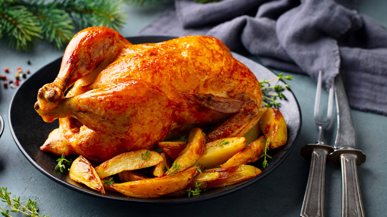 View of whole roasted chicken on a plate with vegetables.