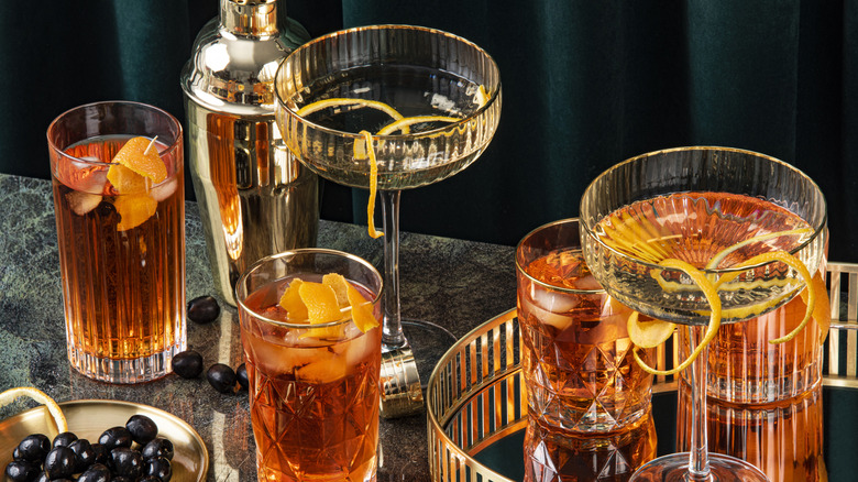 A table with classic cocktails of various sorts on a table with a drink tray and martini shaker.