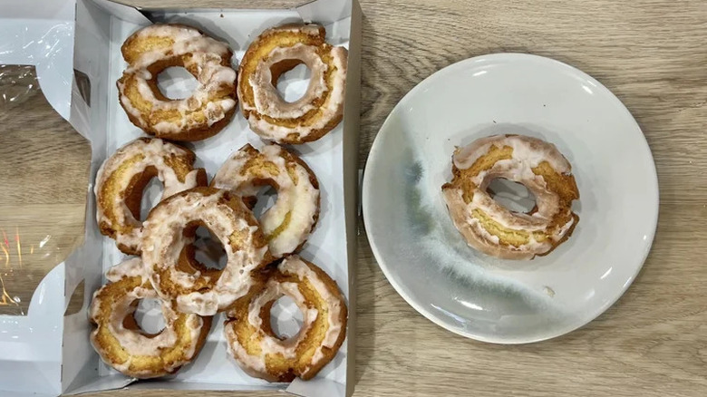 An overhead shot of an box of Glazed Sour Cream Donuts, with one of the donuts sitting on a white plate