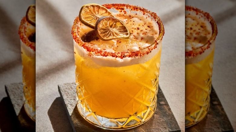 Pineapple margarita in a rocks glass with a Tajìn rim and dry lime wheels used as garnish