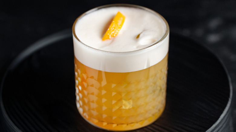 A sour cocktail topped with orange