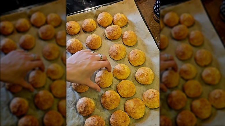 Hand picking up a baked mashed potato ball from a parchment-lined baking sheet