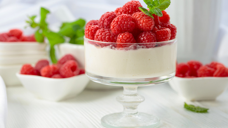 Vanilla panna cotta with raspberries in a glass jar, with raspberries in dishes blurred in the background