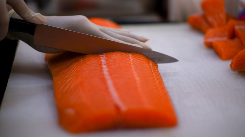 A person wearing gloves slices into a salmon filet