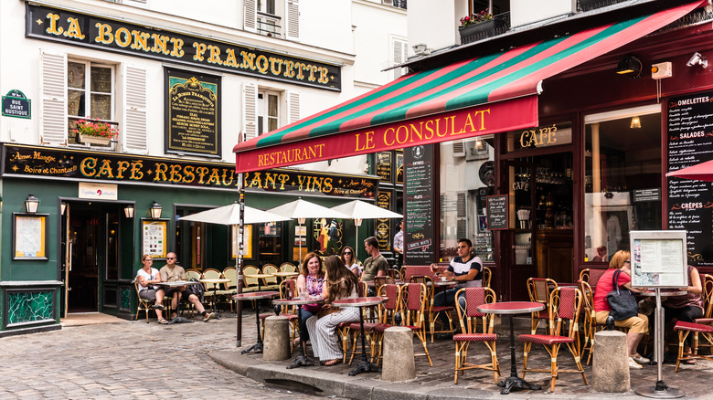 The exterior of two French restaurants, one named La Bonne Franquette, the other named Le Consulat, with tables and chairs arranged outside