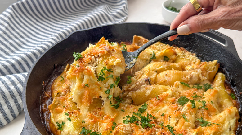 Hand scooping out serving of stuffed shells from skillet