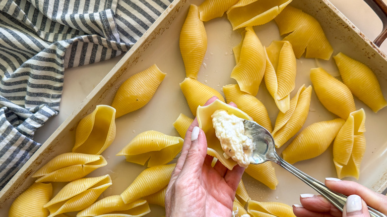 Hand spooning cheese mixture into pasta shell