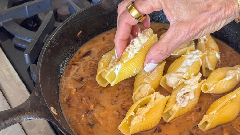 Hand nestling stuffed shells into skillet