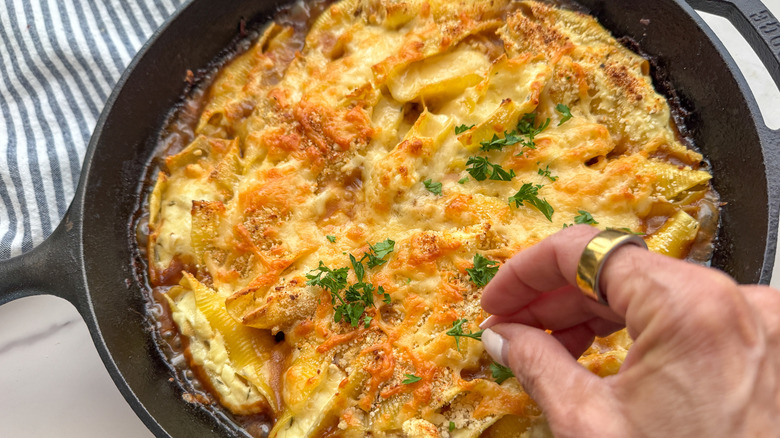 Hand sprinkling parsley over French onion stuffed shells skillet