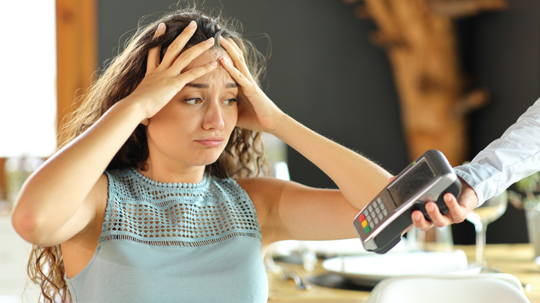 A woman in a restaurant looking unhappy as a waiter hands her a card payment machine