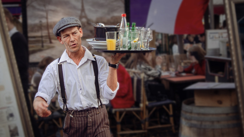 A waiter at a French restaurant wearing traditional clothing and carrying a tray