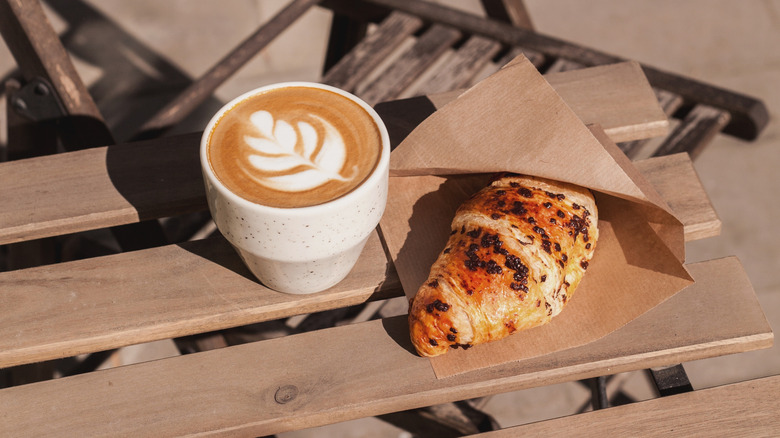 A cup of coffee and a chocolate croissant on a table