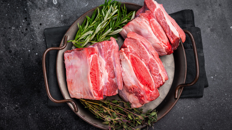 Raw beef short ribs on plate with rosemary sprigs