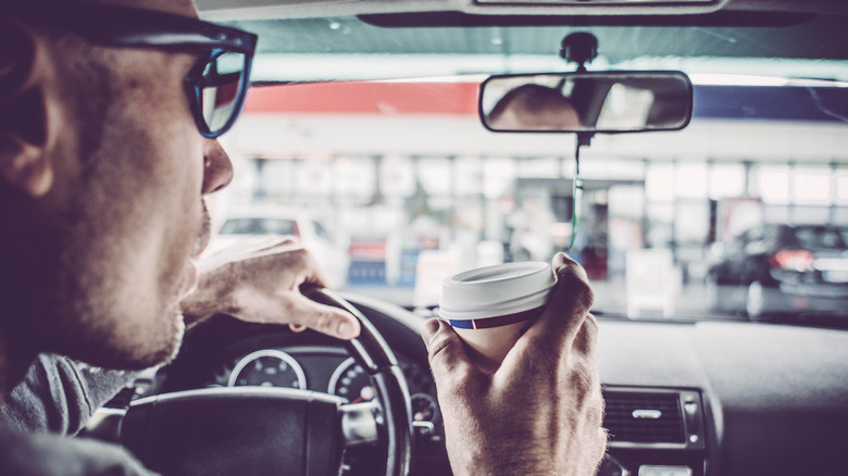 person driving in car drinking coffee at gas station