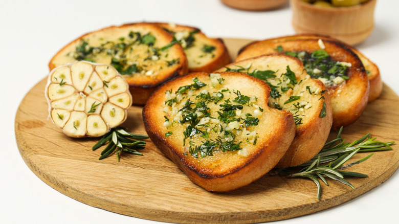 Wooden platter of toasts topped with minced garlic and herbs