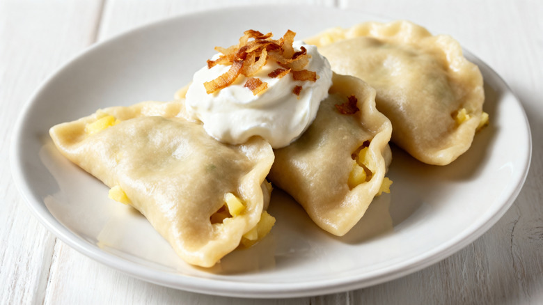Three pierogi on a plate, topped with sour cream and fried onions