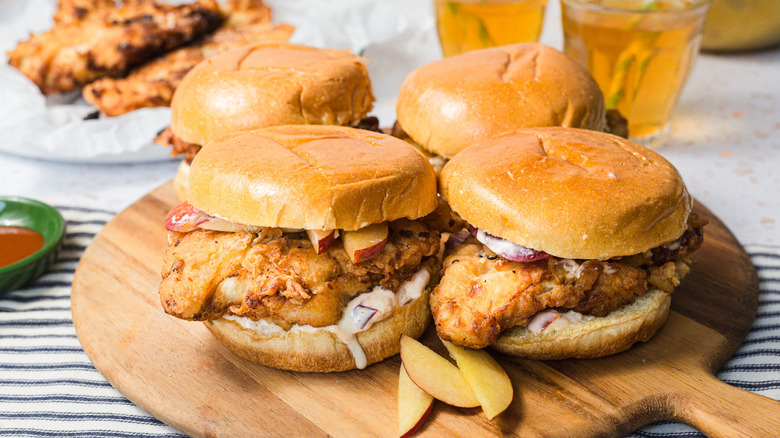 Four fried chicken sandwiches with peaches on a board