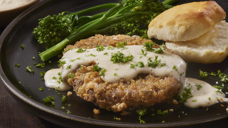 Close-up of Southern fried pork chop on a plate with a biscuit and vegetables.
