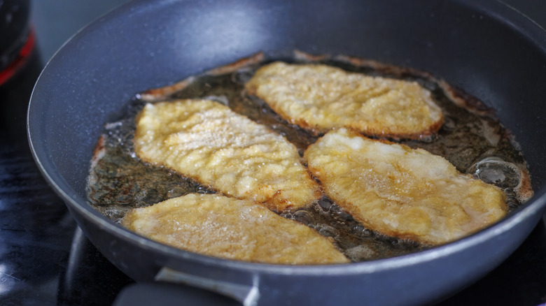 Overhead view of breaded pork chops frying in a pan.