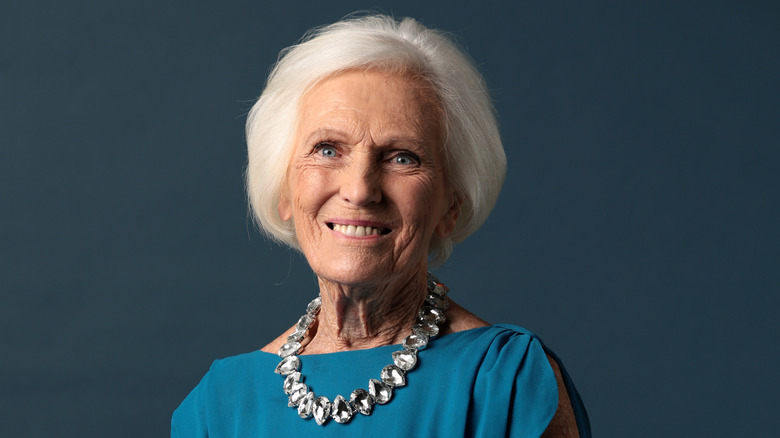 Mary Berry smiling in a blue dress against a dark blue background
