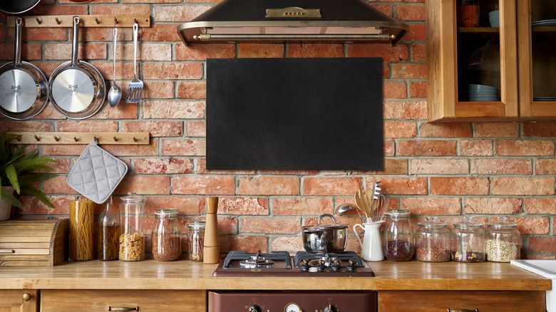 A kitchen with brick walls, hanging pans, and jars of ingredients on the wooden countertop