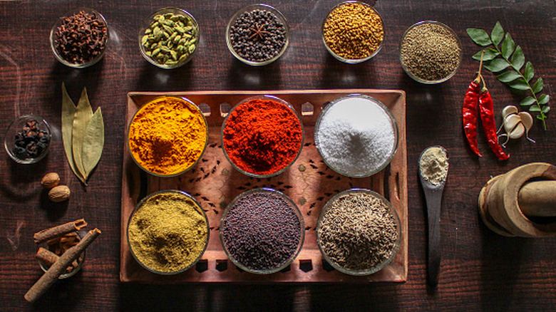 A variety of colorful Indian spices laid out in bowls on a wooden table