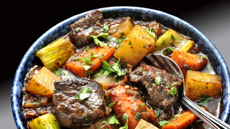 A bowl of beef stew with potatoes, carrots, and celery garnished with fresh herbs