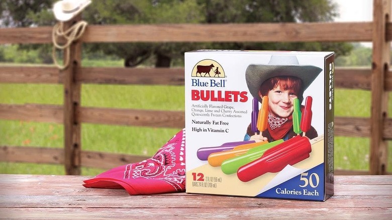 A box of Blue Bell Bullets popsicles sitting on a wooden table next to a red bandana