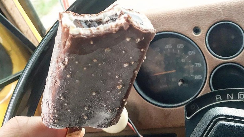 A close-up image of a person holding a Good Humor Candy Center Crunch Ice Cream Bar with a bite taken out of it