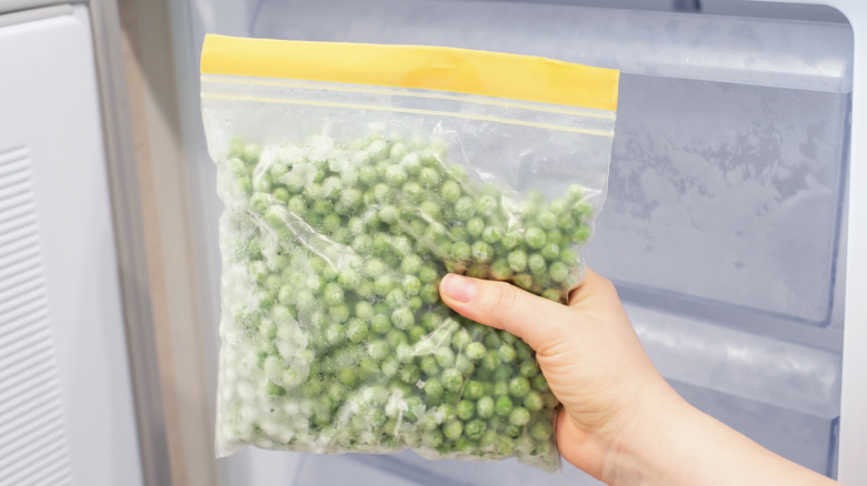 A person holding a freezer bag full of frozen peas in front of a freezer
