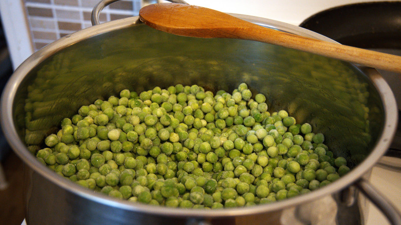Frozen peas in pot with wooden spoon