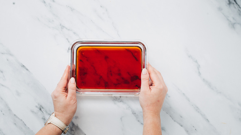 Two hands holding a glass container with the liquid ingredients for a Manhattan cocktail.