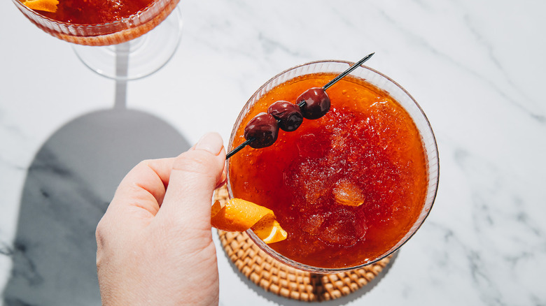 Laying a garnish of three cherries on a coupe glass with a frozen Manhattan cocktail.